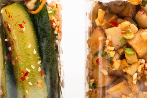 κοντινό πλάνο νόστιμο αγγούρι και daikon ραπάνι kimchi σε γυάλινα βάζα που απομονώνονται σε λευκό - Φωτογραφία, εικόνα