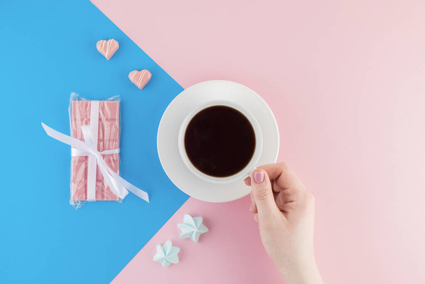 A cup of freshly brewed coffee on beautiful pink and bright blue pastel background. Fresh desserts. Meringue. Pink Chocolate and heart shaped candies. Top view. Flat lay.  - Photo, image