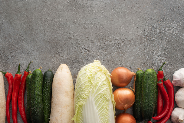 top view of chili peppers, cucumbers, daikon radish, chinese cabbage, onions and garlic on grey concrete background - Фото, изображение