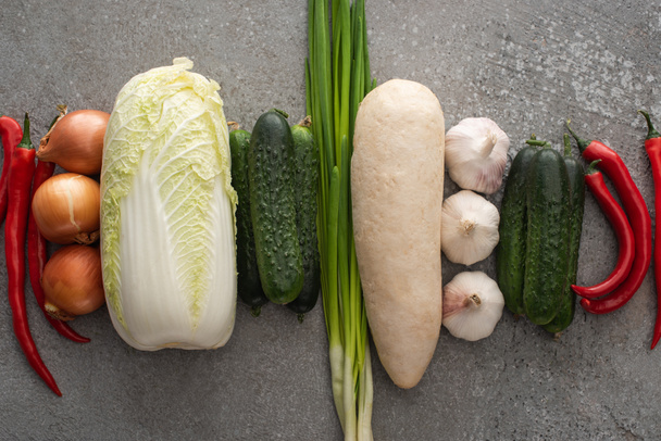 top view of chili peppers, green onions, cucumbers, daikon radish, chinese cabbage, onions and garlic on grey concrete background - Фото, изображение