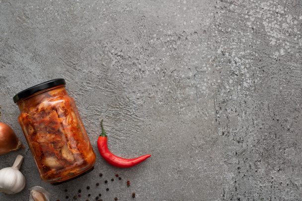 felső kilátás kimchi üveg, chili paprika és fokhagyma beton felületen - Fotó, kép
