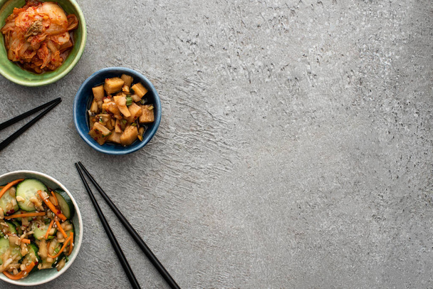 vrchní pohled na mísy s chutnými kimchi v blízkosti hůlek na betonovém povrchu - Fotografie, Obrázek