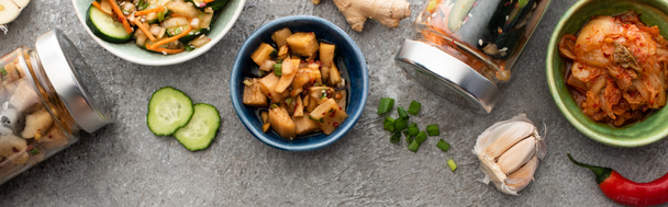 plan panoramique de savoureux kimchi dans des bols et des bocaux près des baguettes, de l'ail et du piment sur la surface du béton
 - Photo, image