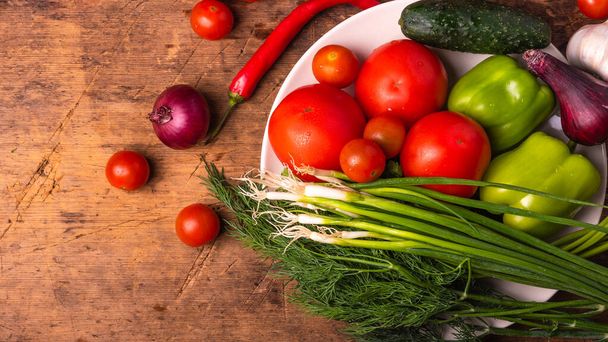 Tomates de verduras frescas, tomates de cereja, pimentas verdes, pimentas, cebolas, pepinos, alho e ervas em uma chapa em uma mesa de madeira rústica - contexto culinário, espaço de cópia, estilo rural, conceito de alimentação saudável
 - Foto, Imagem