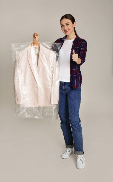 Young woman holding hanger with jacket on light grey background. Dry-cleaning service - Foto, Imagen