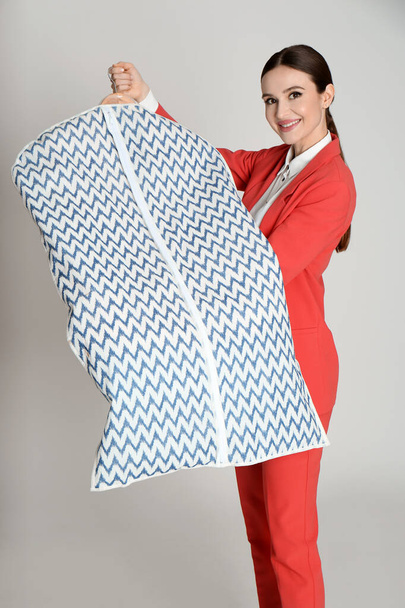 Young woman holding hanger with clothes in garment cover on light grey background. Dry-cleaning service - Фото, зображення