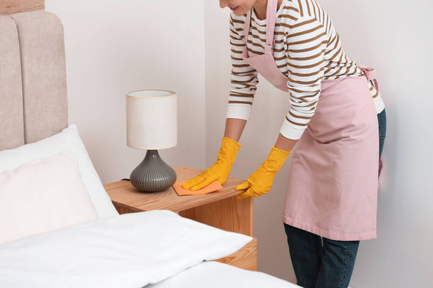 Young chambermaid wiping dust from nightstand in bedroom, closeup - Photo, image