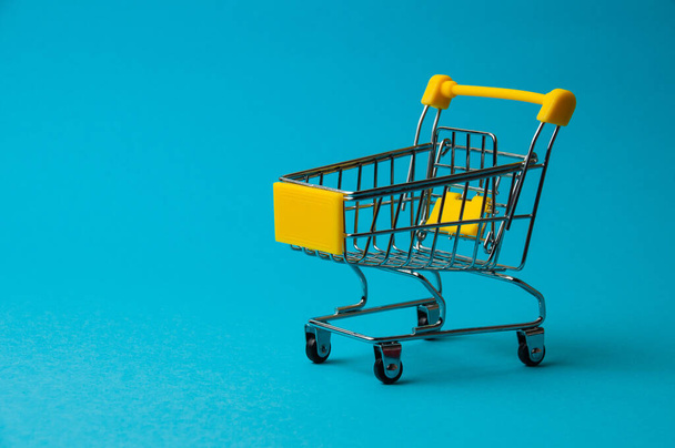 Wózek na zakupy na niebieskim tle. Koncepcja ceny żywności w supermarkecie, zniżki wakacyjne - Zdjęcie, obraz