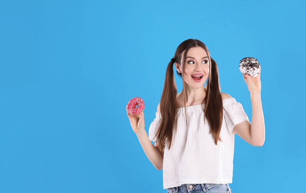 Beautiful young woman with donuts on light blue background - Zdjęcie, obraz