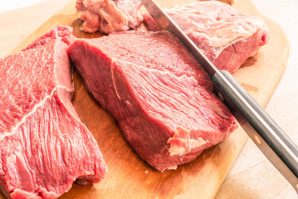 Cutting a piece of beef with a cook's knife on a cutting wooden board close-up - Foto, afbeelding
