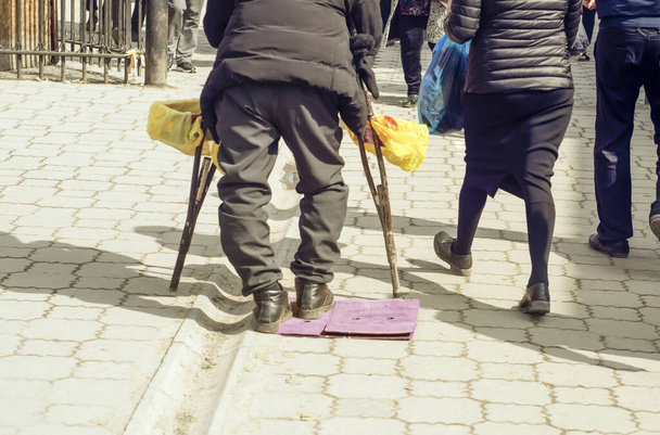 彼の側に松葉杖を持つ障害者の男と市場の中心に彼の手に箱. - 写真・画像