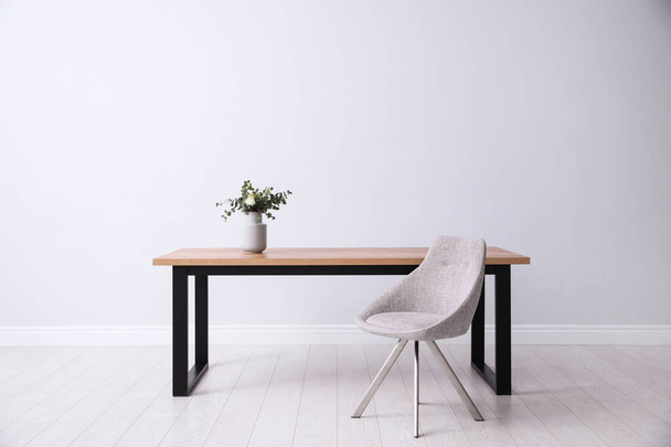 Table and chair near white wall in room. Stylish interior design - Φωτογραφία, εικόνα