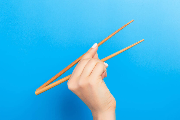 Female hand with chopsticks on blue background. Traditional asian food with emty space for your design. - Photo, Image