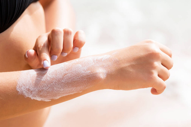 Mooi meisje is het zetten van zon lotion op haar hand op het strand. - Foto, afbeelding