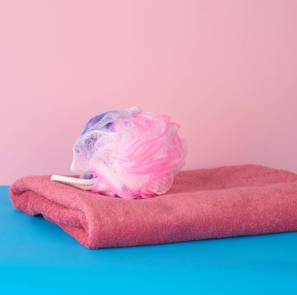 стопка рожевих складених рушників і пластикова мочалка на синьому фоні, набір для ванни
 - Фото, зображення