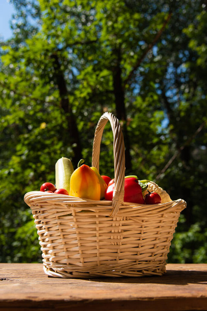 Basket with fresh vegetables on a wooden table in the yard on a background of trees close-up - Photo, Image