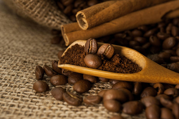 Nahaufnahme, hölzerne Schaufel mit gemahlenem Kaffee und Kaffeebohnen, Zimtstangen auf klebrigem, strukturiertem Hintergrund - Foto, Bild