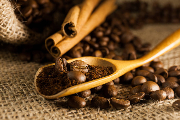 Крупним планом, дерев'яна совок з меленою кавою і кавовими зернами, паличками кориці на тлі мішковини текстурованого фону
 - Фото, зображення