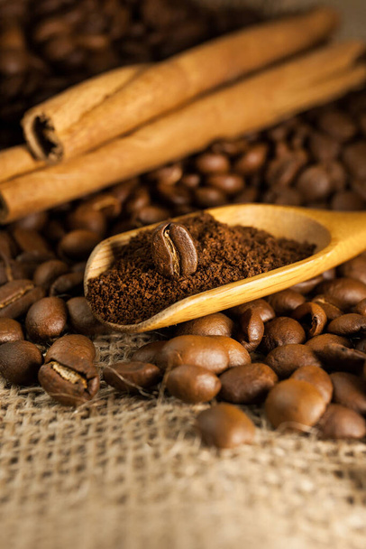 Close-up, wooden scoop with ground coffee and coffee beans, cinnamon sticks on a burlap textured background - Valokuva, kuva