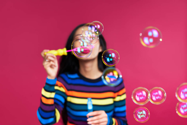 Happy beautiful woman blowing soap bubbles isolated over pink background                    - Photo, Image