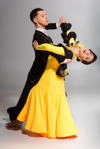 elegant young couple of ballroom dancers dancing on grey - Zdjęcie, obraz