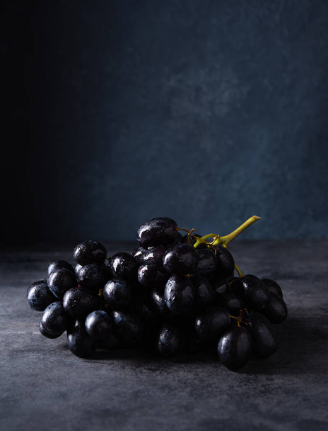 een cluster sappige zwarte druiven ligt op een donkergrijze tafel. Foto donker en humeurig. Vooraanzicht en kopieerruimte - Foto, afbeelding