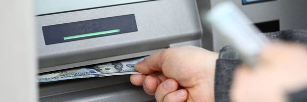 Manos masculinas sosteniendo un montón de billetes de cien dólares en un cajero automático
 - Foto, Imagen