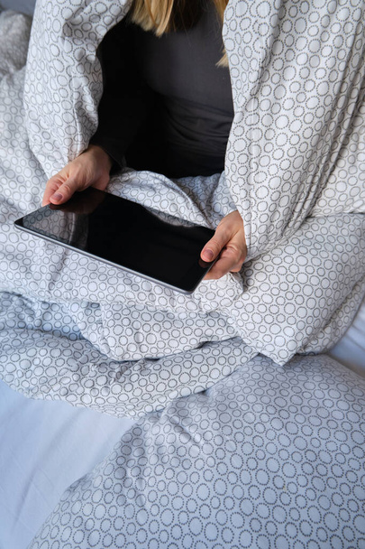 Woman holds tablet in hands. Morning online activities in home. Relax in bed, watching movies and TV shows on mobile device. Social media addiction. Work at home, freelance. Technology in lifestyle - Foto, imagen