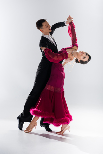 elegant young couple of ballroom dancers in red dress in suit dancing on white - Фото, зображення