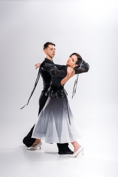 elegant young couple of ballroom dancers in black outfit dancing on white - Photo, Image