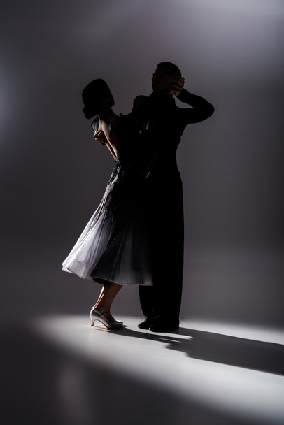 elegant young couple of ballroom dancers in black outfit dancing in dark - Fotoğraf, Görsel