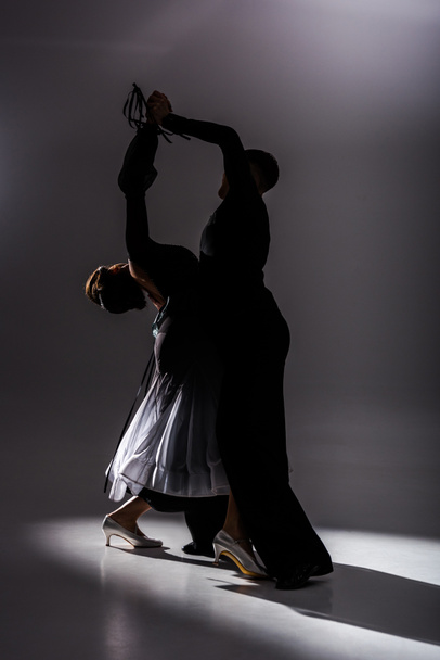 elegant young couple of ballroom dancers in black outfit dancing in dark - Photo, image