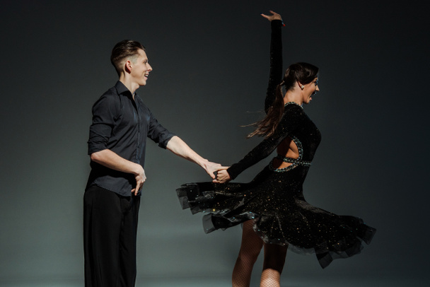 elegant young couple of ballroom dancers in black outfits dancing in dark - Photo, Image