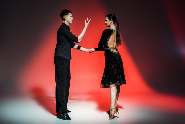 elegant young couple of ballroom dancers in black outfits dancing in red light - Zdjęcie, obraz