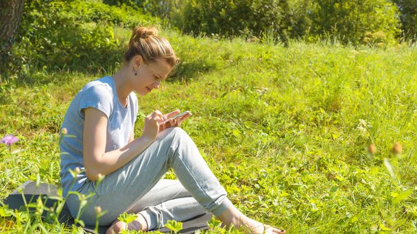 Jovem mulher feliz atraente lê mensagens no smartphone em um prado de montanha - conceito de férias na natureza
 - Foto, Imagem