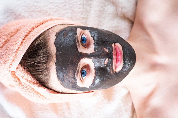 Rosto de mulher jovem atraente com máscara cosmética de barro preto - conceito de tratamentos de beleza em casa
 - Foto, Imagem