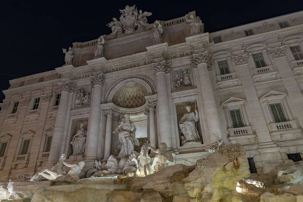 Nocne zdjęcie oświetlonej Fontanny di Trevi, Rzym, Włochy. Najsłynniejsza późnobarokowa rzymska fontanna. Rzeźby z białego marmuru w wodzie. - Zdjęcie, obraz