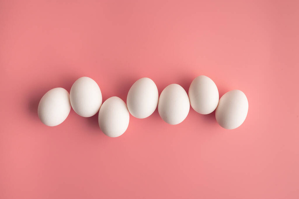 白鶏の卵のパステルピンクの背景に行に配置されます。要約創造的なミニマリストフラットレイイースターのコンセプト. - 写真・画像