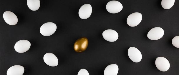 Creative pattern made of natural white chicken eggs and one golden painted egg on black background. Diversity, individuality concept. Flat lay overhead shot. - Photo, Image