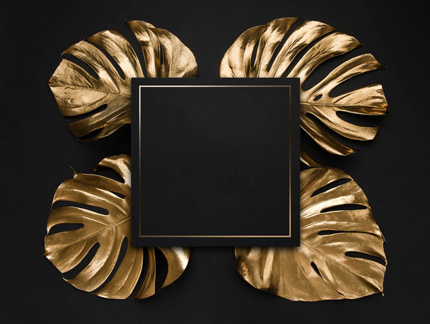 Natural monstera leaves spray painted with golden metallic paint on dark deep black background. Trendy layout border frame wtih blank card as coopy space. Creative luxury cover, invitaion template. - Fotoğraf, Görsel