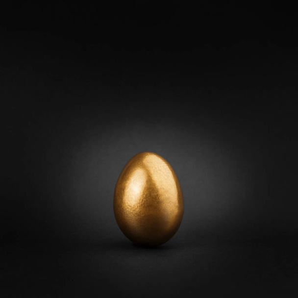 Einzelne goldglänzende Spray bemalte Ei auf abstrakten schwarzen minimalen Hintergrund isoliert. Luxus simuliert Osterferien Konzept. Leerer Raum, Raum für Text, Kopie. - Foto, Bild
