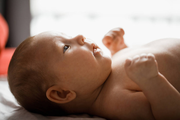 Κοντινό πλαϊνό προφίλ backlit πορτρέτο του μωρού που βρίσκεται στο κρεβάτι στην πλάτη της - Φωτογραφία, εικόνα