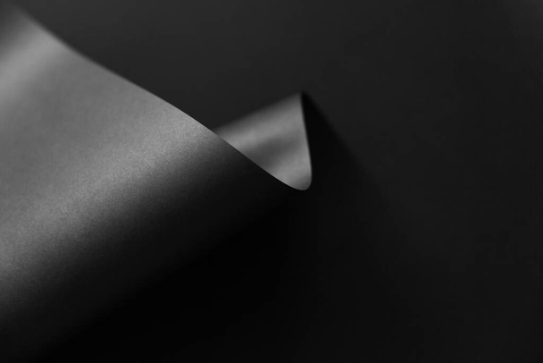 Διπλωμένο μαύρο μονόχρωμο χαρτί σε σκούρο φόντο. Καλλιτεχνικό γεωμετρικό σχέδιο μόδας. - Φωτογραφία, εικόνα