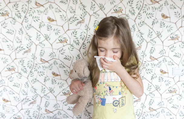 Une petite fille d'âge préscolaire éternue dans une serviette parce qu'elle a attrapé un rhume et a un nez bouché et un nez qui coule. Allergie aux poils et au pollen chez l'enfant. L'enfant est tombé malade de la grippe
. - Photo, image