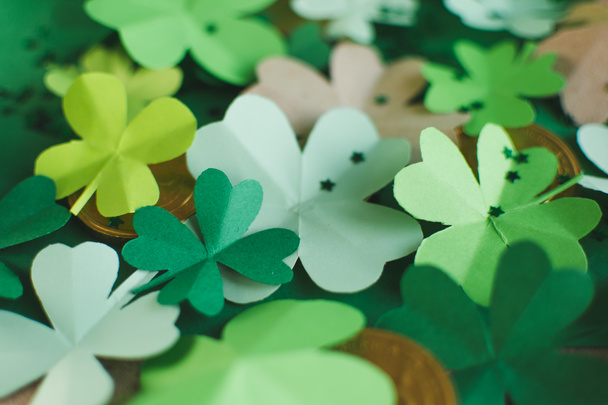 Top view of different shades of green four-leafed paper shamrocks with chocolate coins arranged in chaotic order. Saint Patricks day and lucky concept - Photo, Image