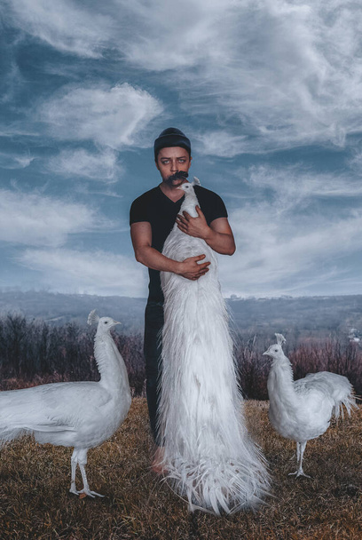 Hombre con pavo real blanco en la naturaleza
 - Foto, Imagen
