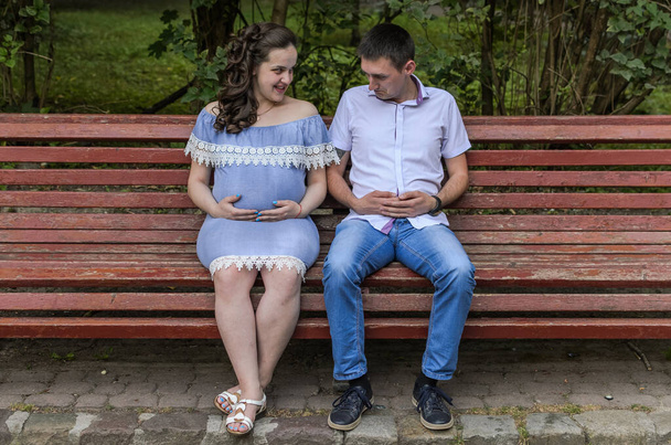 Young couple in love, husband and pregnant wife on a bench in the park, happy family - Fotografie, Obrázek