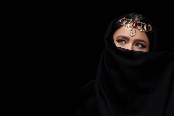 Um retrato conceitual do Oriente Médio do rosto de uma mulher decorada com jóias de estilo oriental em um fundo de estúdio preto
. - Foto, Imagem