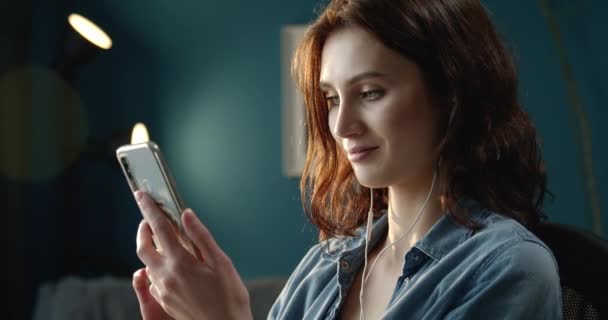 Smiling woman using smartphone while sitting at home - Materiał filmowy, wideo