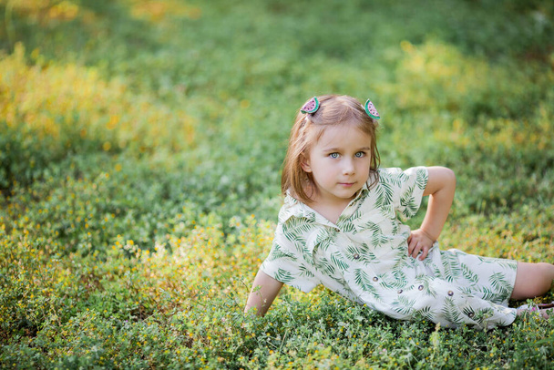 Piccola ragazza carina è seduta sull'erba. Ragazza felice al parco. Estate
. - Foto, immagini